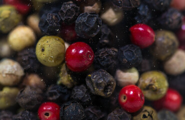 Variety of black, red green dried pepper seeds in a glass jar macro shot.