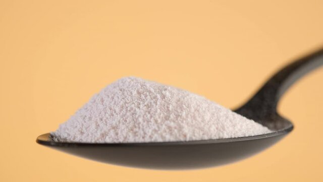pouring collagen powder in black spoon, yellow background. Natural beauty and health supplement
