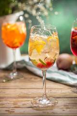 Fresh lemonade cocktail with orange, cherry and ice in wine glass splash on wooden table