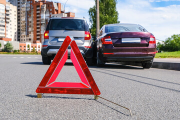 Triangular red retro-reflective sign of accident on the road. Collision of two cars. Broken bumper and hood. Car accident on the street