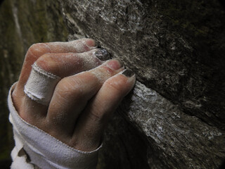Rock climbers fingers holding on to a crimp on rock, while bouldering, with chalk and tape on hand. Hanging on to the edge of a rock, close-up.