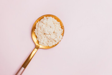 White powder in a spoon on pink background.
