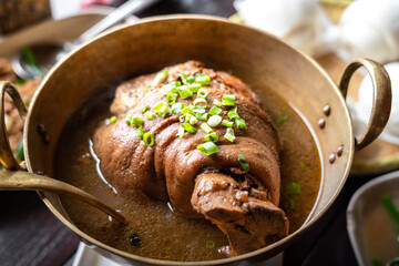 A large pork leg stewed that cooked by traditional Chinese recipe and ingredients is served in the metallic pot, placed on restaurant's table. Food photo.