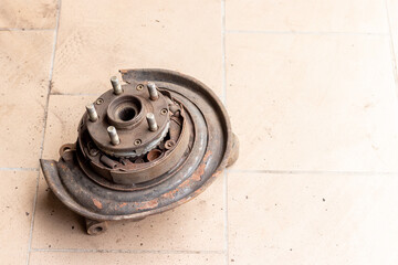 Old, used, rusty rear hub, on which the brake pads of the parking brake are visible, without brake disc on the beige tiled floor of the workshop