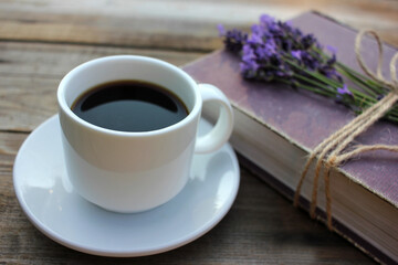 Cup of coffee and old book decorated with lavender flowers and tied with jute twine on wooden table. Copy space. Selective focus. Enjoying summer life
