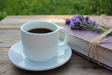 Cup of coffee and old book decorated with lavender flowers and tied with jute twine on wooden table. Copy space. Selective focus. Enjoying summer life
