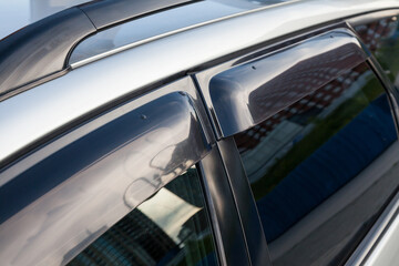 Close-up of the side windows of a car sedan with plastic darkened pads protecting against wind and rain when the window is open. Element of light tuning of a gray sedan.