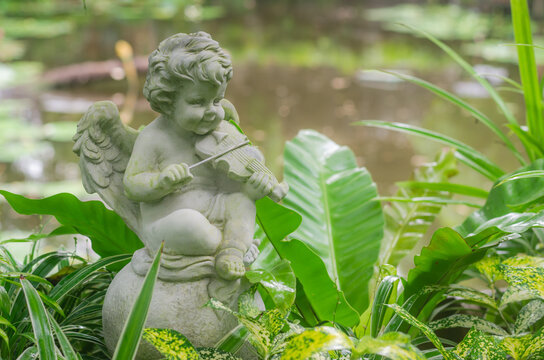 Figurine of  a little  angel cupid playing the violin in the garden.