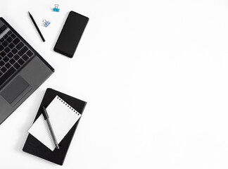 Minimalistic workplace in white and black colors: laptop, phone, pen, notebook on a white background with copy space 