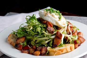 Salad. Frisee lettuce dress with olive oil and balsamic vinegar and topped with bacon lardons a fried egg and garnished with italian parsely and a toasted baguette. Served in a French Bistro.