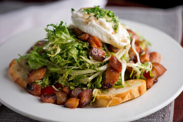 Salad. Frisee lettuce dress with olive oil and balsamic vinegar and topped with bacon lardons a fried egg and garnished with italian parsely and a toasted baguette. Served in a French Bistro.