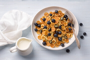 Plate of Mini Pancakes cereals with cream, honey and berries on a light blue background. trendy food. homemade breakfast. top view