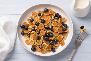 Plate of Mini Pancakes cereals with cream, honey and berries on a light blue background. trendy food. homemade breakfast. top view