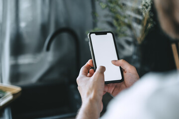 Man using a smartphone with a white blank screen in the kitchen. 