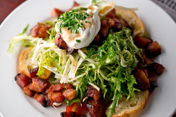 Salad. Frisee lettuce dress with olive oil and balsamic vinegar and topped with bacon lardons a fried egg and garnished with italian parsely and a toasted baguette. Served in a French Bistro.