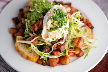 Salad. Frisee lettuce dress with olive oil and balsamic vinegar and topped with bacon lardons a fried egg and garnished with italian parsely and a toasted baguette. Served in a French Bistro.