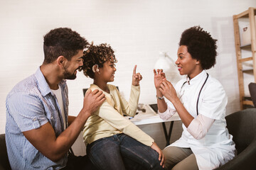 Smiling deaf african american girl with ear implant at doctor's office.