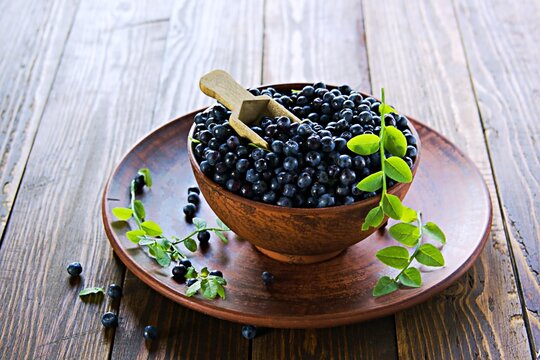 Fresh wild blueberries in a clay brown bowl on a wooden background. Healthy food, snacks.