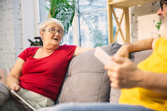 Wondered. Couple of seniors spending time together being quarantined - caucasians mature and retired man and woman using modern gadgets, talking, drinking tea. Eyes tired of gadget's life. Lifestyle.
