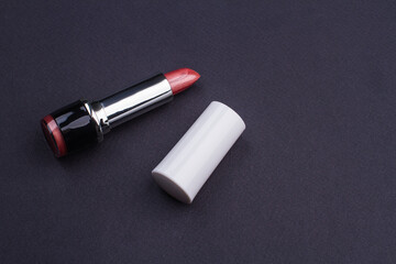 Pink open lipstick in a tube on black background. Cosmetics, makeup and beauty concept. White cap casing.