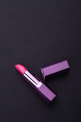 Violet lipstick and cap on black background from top. Flat composition of women cosmetics.