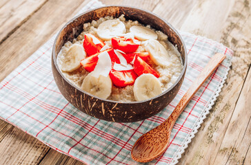 Quinoa porridge with coconut milk and fresh strawberries in a coconut bowl wooden rustic background. Healthy Lactose and Gluten Free Breakfast.