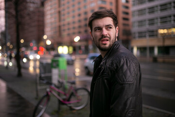 Back view of a handsome frowning young man walking down the street turning back in the rain, wear in jacket.