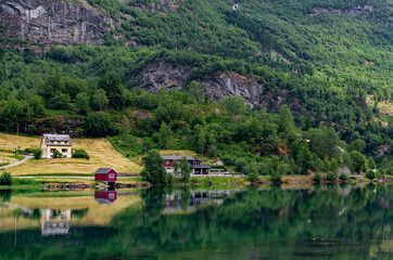 Fototapeta na wymiar Beautiful Norwegian landscape reflected in mirror like water surface of a lake. Farm houses, forest, fields and mountains on a bank of the lake Floen, Oldedalen valley, Norway.