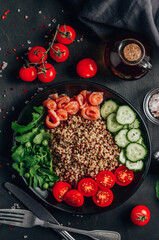 Salmon Poke bowl. Raw fish salad with quinoa, cucumber, tomato and arugula. Asian trendy food on black wooden background. Top view. Vertical photo