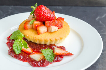 Homemade cheese cakes served with strawberry sauce made from organic strawberries. Topping with fresh organic strawberries and decorated with mint leaves.