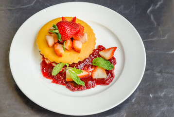 Homemade cheese cakes served with strawberry sauce made from organic strawberries. Topping with fresh organic strawberries and decorated with mint leaves.