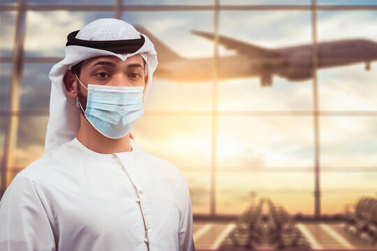 Arabic traveler business man wearing mask waiting to board into airplane, standing in departure terminal in airport.  Arab passenger traveling by plane transportation during covid19 virus pandemic.