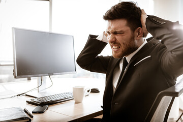 Business crisis concept. Emotional young businessman at work. Worried stressed manager sitting at...
