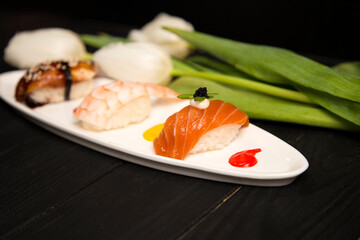 Set of Japanese Nigiri Sake Sushi with salmon in focus near nigiri Ebi with shrimp and Unagi with eel. colourful food decoration painting spots on plate near white tulips. Asian restaurant menu
