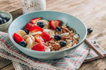 Healthy breakfast bowl with oat granola with dried buckwheat, nuts and coconut chips, berries and rice milk on a rustic background. Selective focus