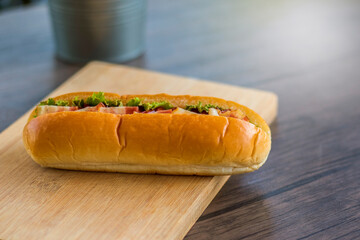 Sausage sandwich with ham, cheese, bacon, lettuce, wooden table top