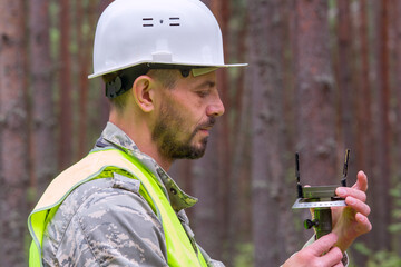 Forest engineer works with a geodetic tool. Forester in helmet and working uniform.