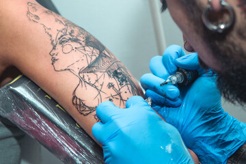 A tattoo artist paints a client's tattoo with ink. Tattoo artist holding a tattoo machine in Blue Sterile Gloves.