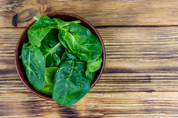 Ceramic bowl with spinach leaves on rustic wooden table. Top view