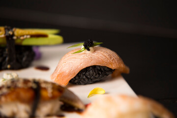 Set of Japanese nigiri. Close up of Salmon Sake Tataki with black rice, mayonnaise, flying fish roe (Tobiko caviar) in focus. Decorated food plate on dark wooden background. Asian restaurant menu
