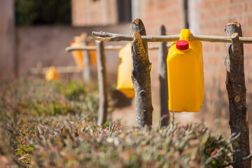 Gallons of water recycled and adapted hanging from tree logs as water taps stations for students to wash their hands on classroom doors in Africa. Also known as tippy taps