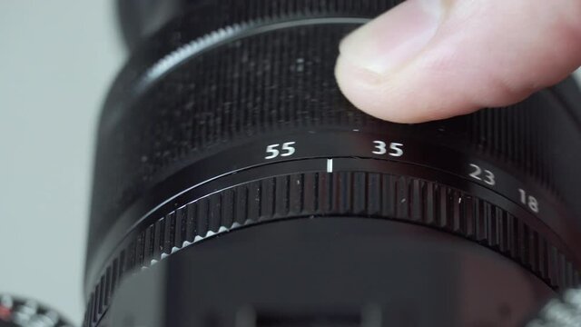Male fingers adjusting zoom on black digital mirrorless camera lens close up