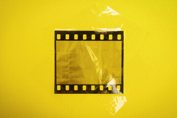 Fototapeta premium original 35mm film strip or snip with cello tape von yellow background, empty film cell or frame, macro photo, no scan 