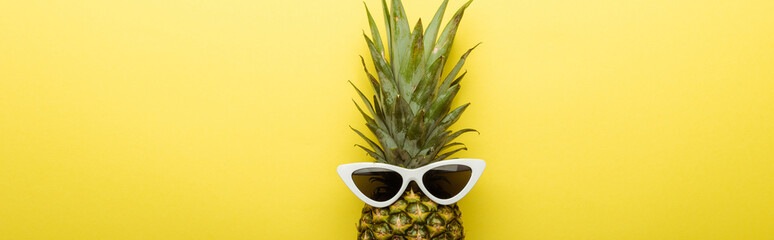 top view of ripe pineapple in sunglasses on yellow background, panoramic shot