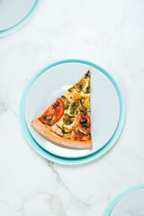 Slice of Vegan vegetable pizza. Food on pastel turquoise and gray serving plates. tableware on marble background. Dish with tomatoes, eggplant, champignons, Mozzarella cheese and basil pesto sauce. 

