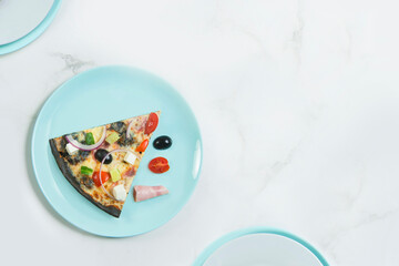 Slice of meat pizza with vegetables. Dish with cherry tomatoes, cucumber, Feta cheese, ham, black olives and Spanish onion on black dough. ingredients on pastel serving plate, marble background.
