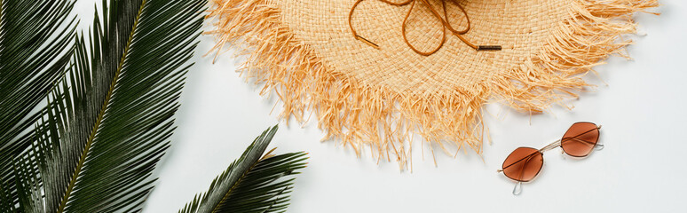 top view of green palm leaves, straw hat and sunglasses on white background, panoramic shot