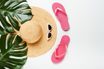 top view of green palm leaves, straw hat, sunglasses and flip flops on white background