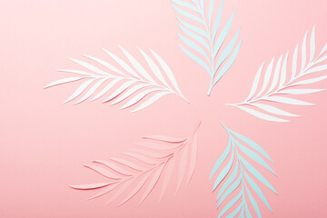 top view of white, pink and blue paper cut palm leaves on pink background