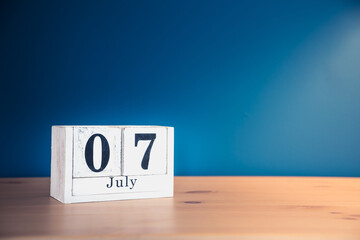 July 7 - white calendar blocks on wooden table against vintage blue background